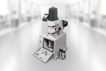 Single-toggle crusher / jaw crusher EB150x100 TL in the laboratory. The device's grinding chamber is open, 2 sub-units are next to the device. The smartphone with app control is switched on and ready for operation