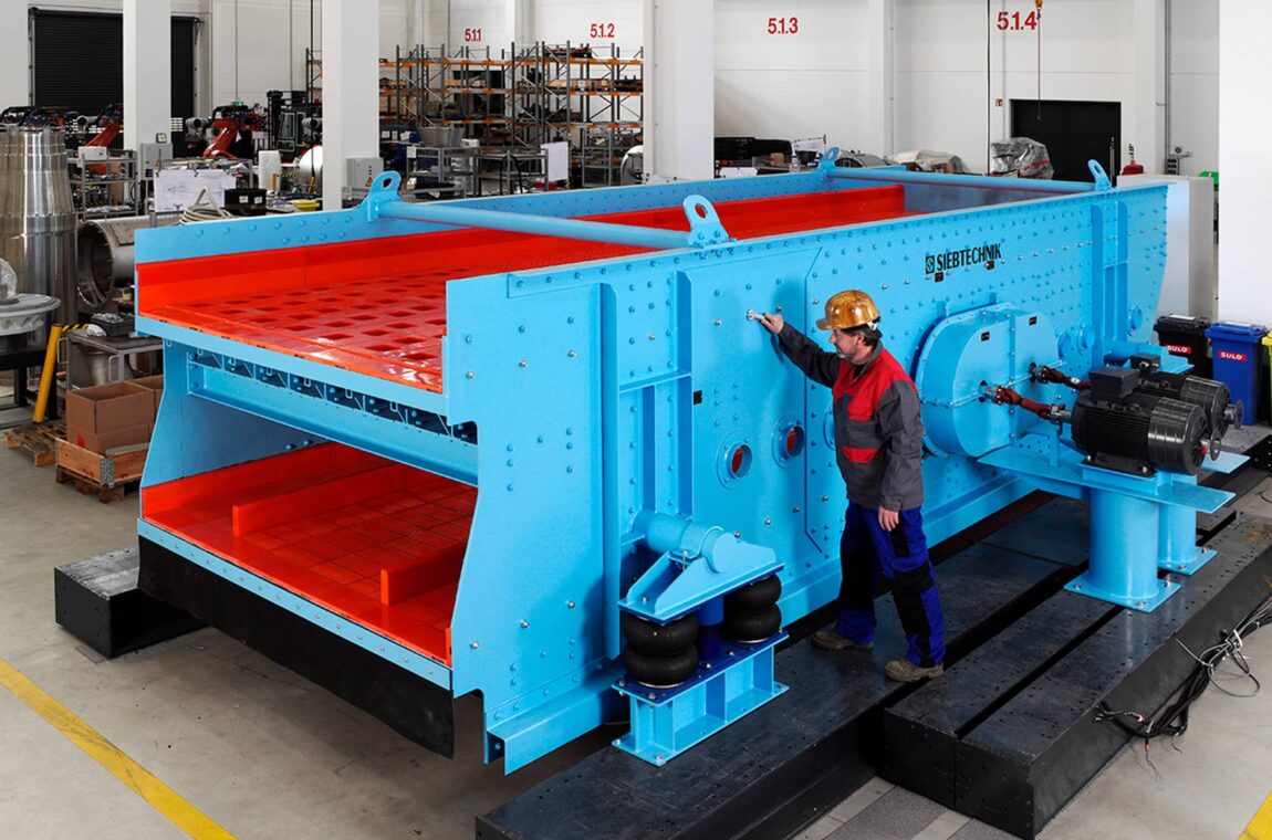 Elliptical vibrating screening machine type E24-70 - fitter checks final details. The machine has 2 screen decks and polyurethane screen linings