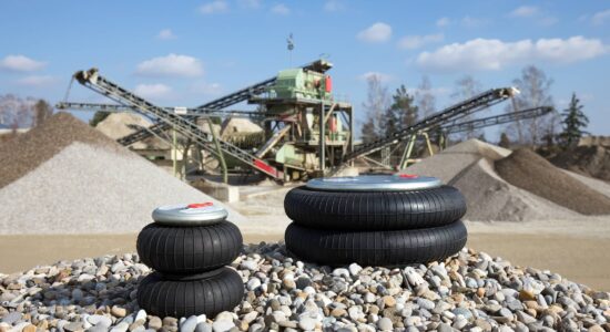 Two individual, differently sized air bellows of the LuCoTec air suspension system lie on a pile of gravel in a gravel works, in the background you can see the plant with screening machines and conveyor system